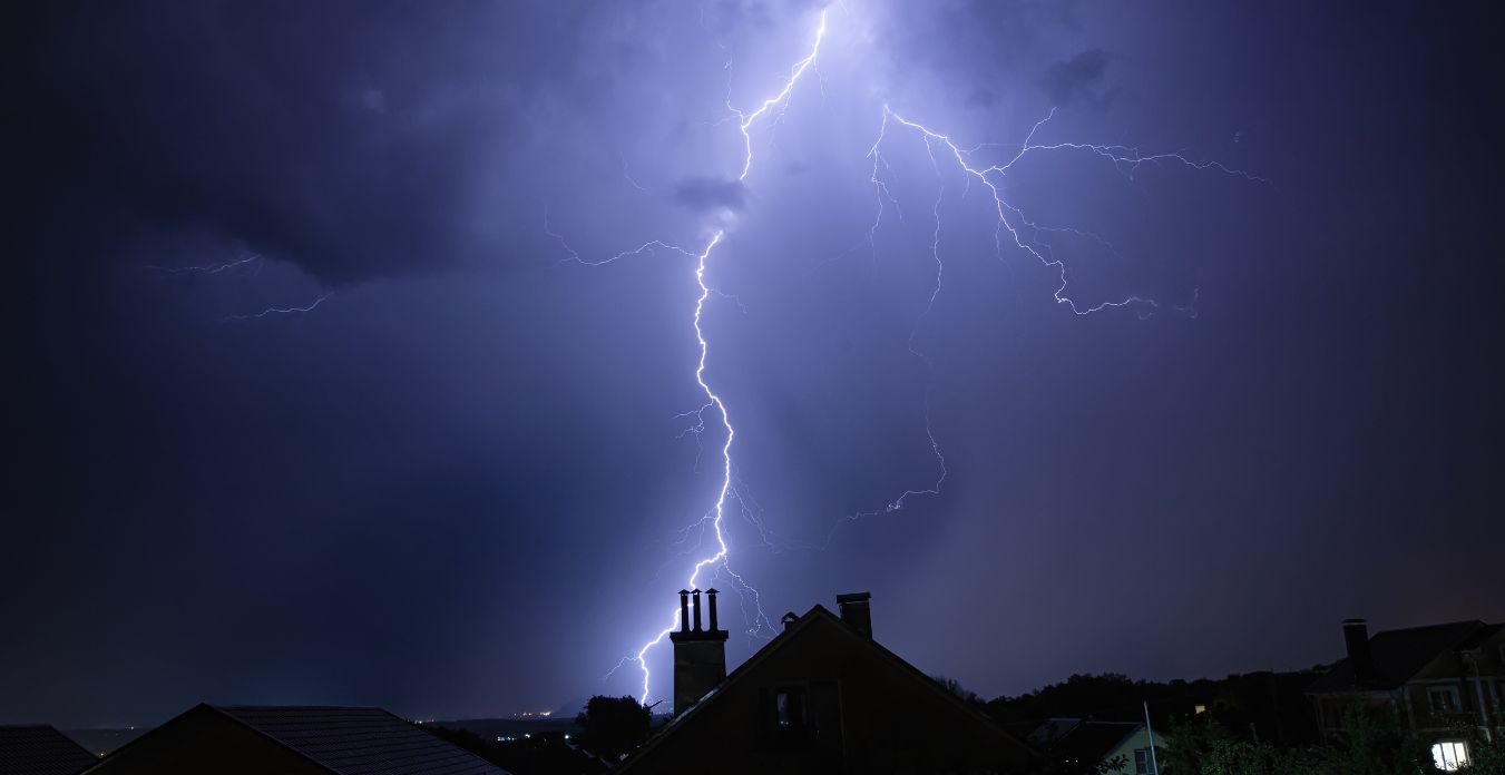 A lightning bolt illuminates a suburban skyline at night